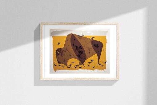 Framed artwork of a stylized American bison in shades of brown against a golden yellow background, surrounded by small blackbirds in flight. The frame is light wood, displayed against a neutral wall with sunlight creating soft shadows on the left side.