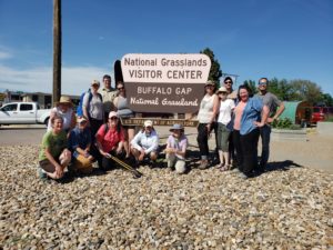 A group of people of all ages posing for a picture next to the National Grasslands Visitor Center, Buffalo Gap National Grassland sign
