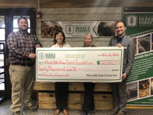 Matt White-BHPFA Retail Operations Manager, Patty Ressler-BHPFA Executive Director, Mary Laycock-BHPFA Board President, Chris Huber-BHACF Donor Relations Manager are holding a large check in front of a sign for Black Hills Parks & Forests Association