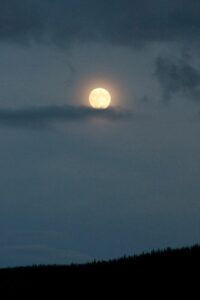 Hazy pale orange full moon with clouds on a gray sky over a silhouette of a hillside