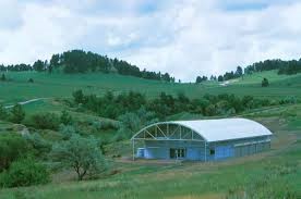 Blue rectangular building with domed roof in a low spot within a lush green prairie valley.