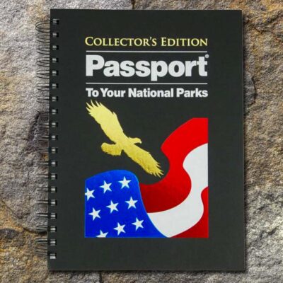 Spiral-bound black cover book lies on stone surface. Text on cover reads Passport to Your National Parks Collectors Edition.