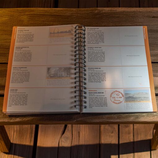 Open spiral-bound national park passport book displayed on a wooden table. The pages feature detailed descriptions of various national parks and monuments, along with designated spaces for collecting stamps. One stamp, dated August 12, 2024, is visible on the page for Agate Fossil Beds National Monument in Nebraska. The layout is organized with text, images, and stamp areas, designed for documenting visits to different national park sites across the United States. Sunlight softly illuminates the pages, creating a warm, inviting atmosphere.