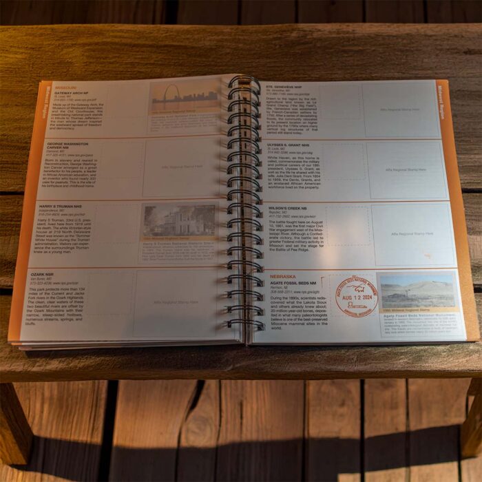 Open spiral-bound national park passport book displayed on a wooden table. The pages feature detailed descriptions of various national parks and monuments, along with designated spaces for collecting stamps. One stamp, dated August 12, 2024, is visible on the page for Agate Fossil Beds National Monument in Nebraska. The layout is organized with text, images, and stamp areas, designed for documenting visits to different national park sites across the United States. Sunlight softly illuminates the pages, creating a warm, inviting atmosphere.