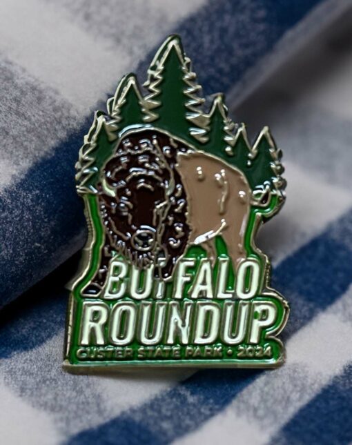 2024 Buffalo Roundup Custer State Park pin with a brown bison in front of green pins on a shiny metallic pin.