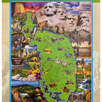 Front of a 1000-piece jigsaw puzzle box titled 'The Black Hills National Forest.' The design features a detailed map of the Black Hills National Forest surrounded by illustrations of iconic landmarks, wildlife such as bison and mountain lions, and notable attractions like Mount Rushmore and Devils Tower. The title is in bold orange and green, with '1000 Jigsaw Puzzle' written in the upper right corner.