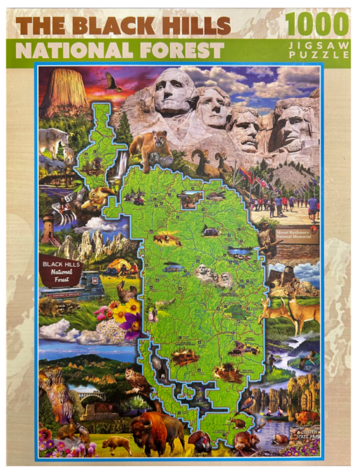 Front of a 1000-piece jigsaw puzzle box titled 'The Black Hills National Forest.' The design features a detailed map of the Black Hills National Forest surrounded by illustrations of iconic landmarks, wildlife such as bison and mountain lions, and notable attractions like Mount Rushmore and Devils Tower. The title is in bold orange and green, with '1000 Jigsaw Puzzle' written in the upper right corner.