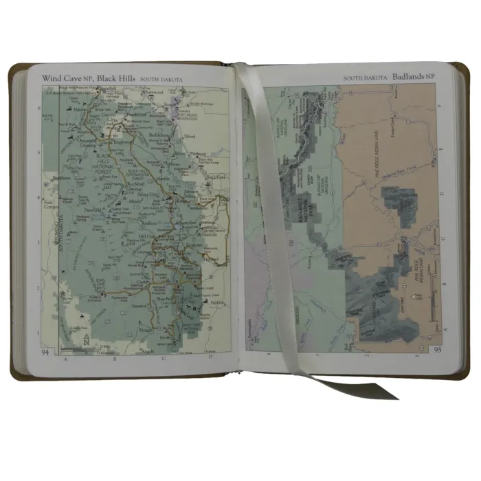 Open leather-bound atlas showing detailed color maps of Wind Cave National Park and Badlands National Park in South Dakota.