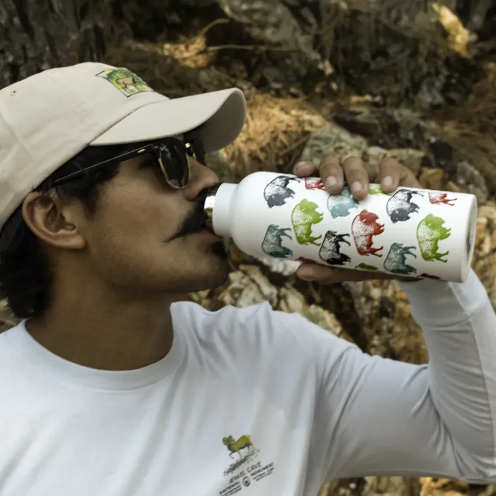 Person drinking from a white stainless-steel water bottle patterned with red, green, teal, and black bison silhouettes, shown outdoors.