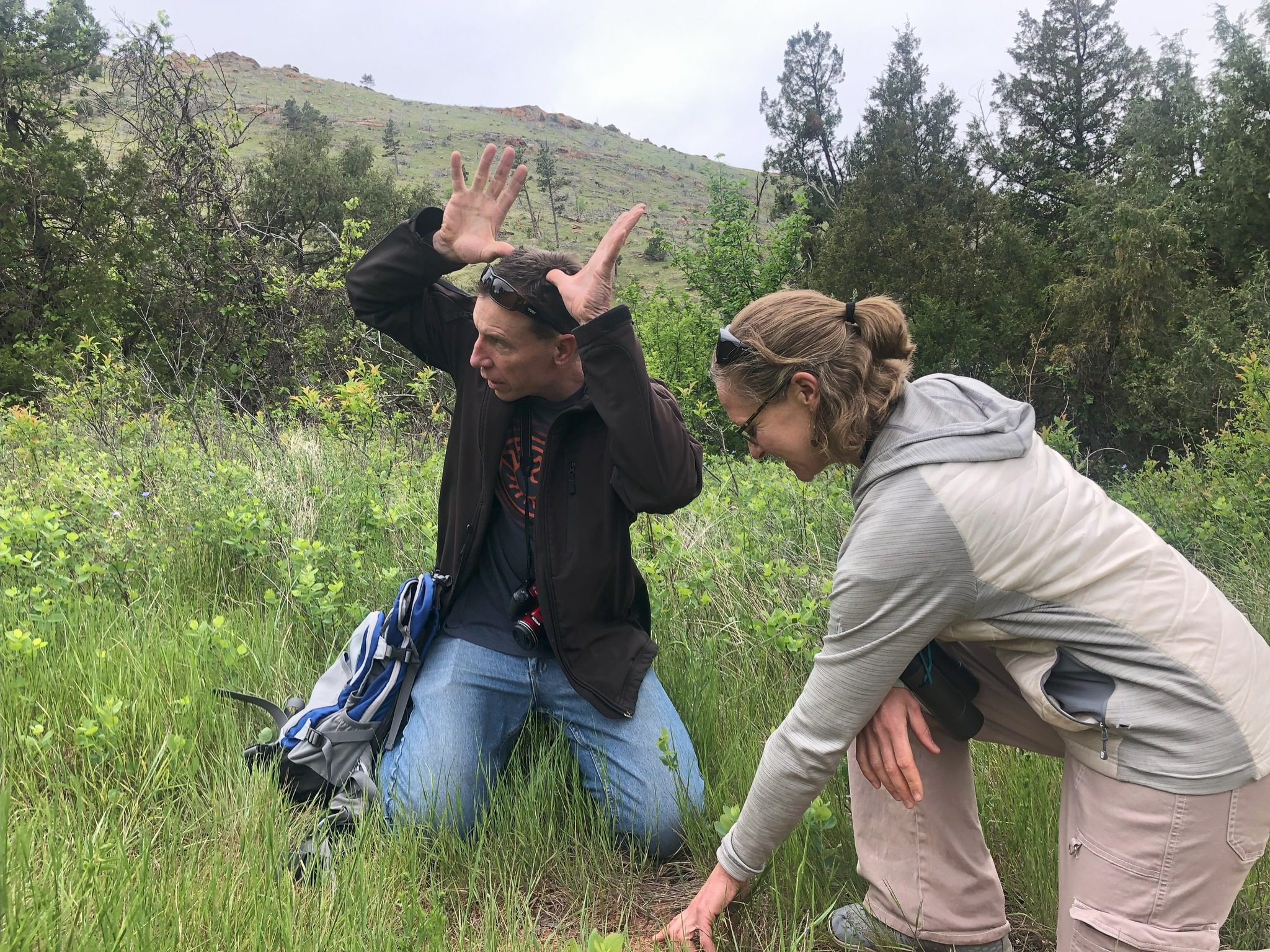448146428_855889863233473_8751069587192682187_n A man and a woman kneeling in grass. The woman is pointing at something in the dirt.