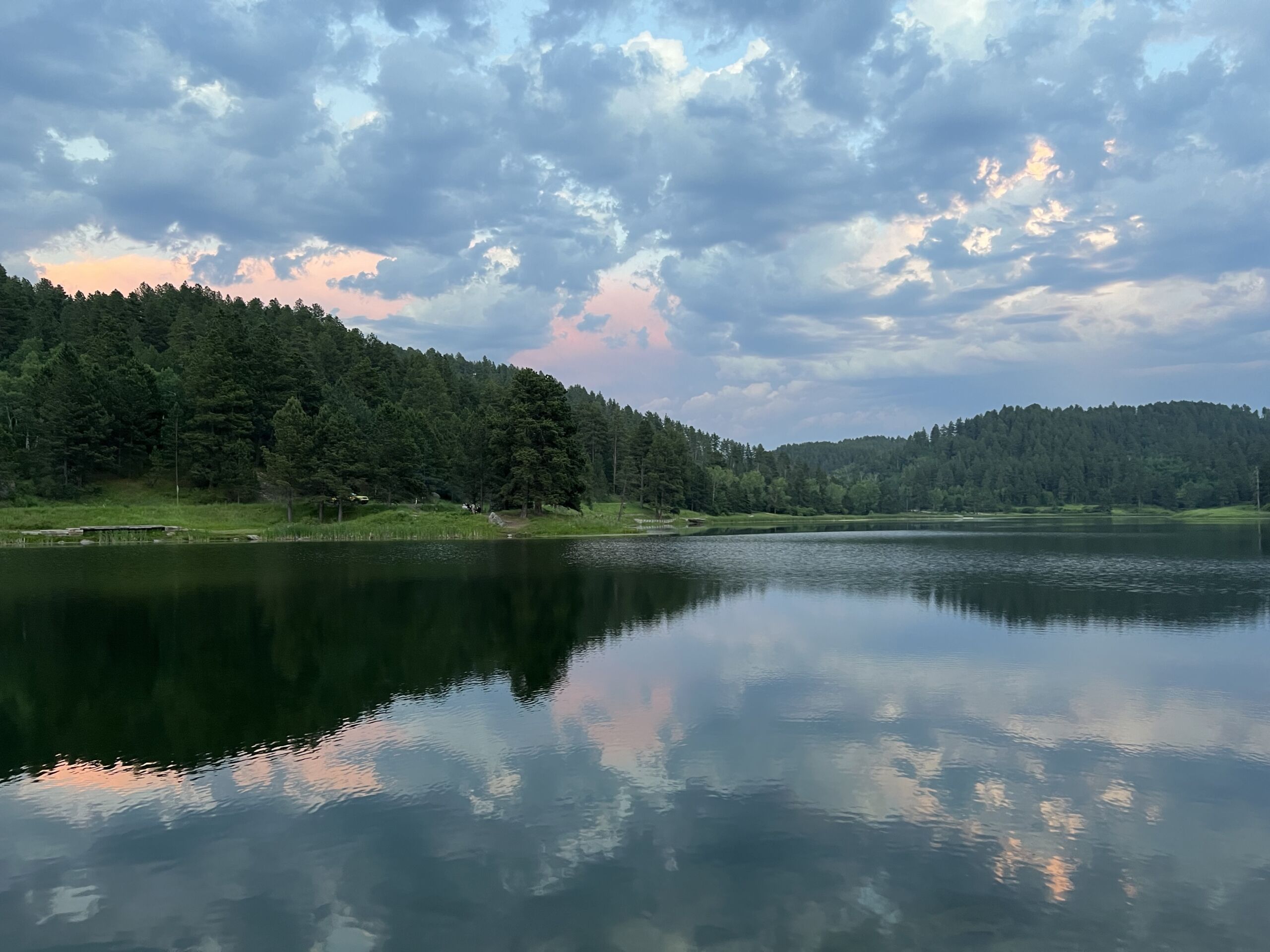 IMG_0294 A mountain lake with dark green pines on the edge, with a clouded sunset