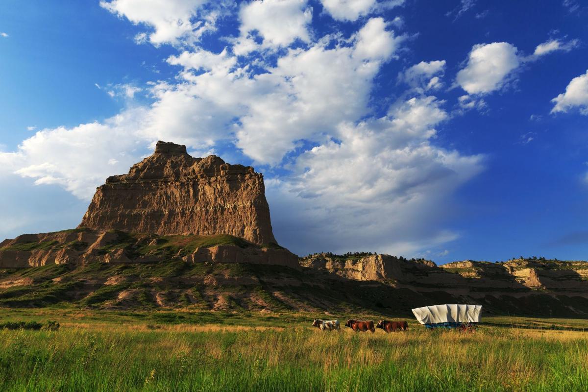 Scotts Bluff with green grassy field in foreground and blue sky with puffy clouds above