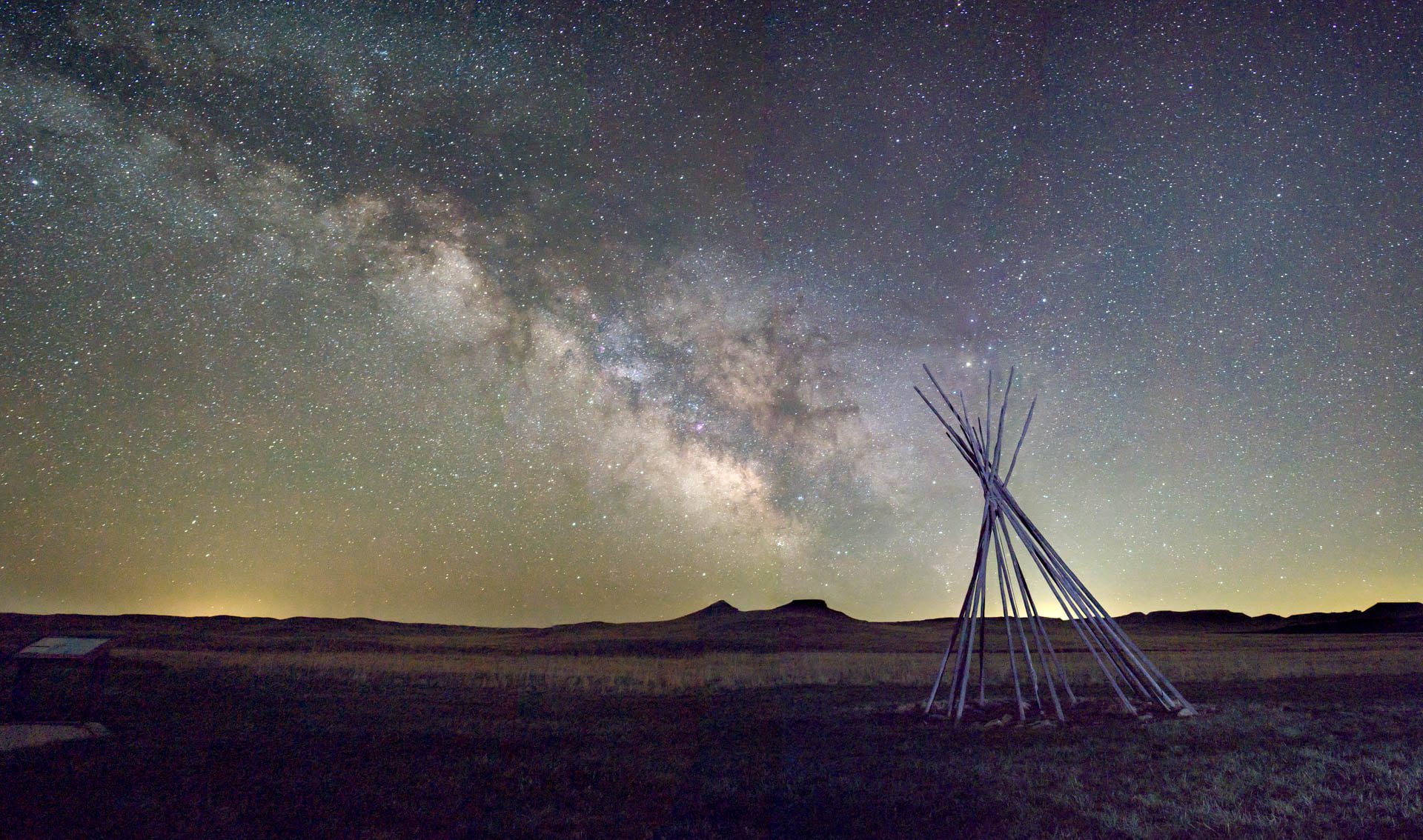 Tipi poles with the milky way rising above hills beyond