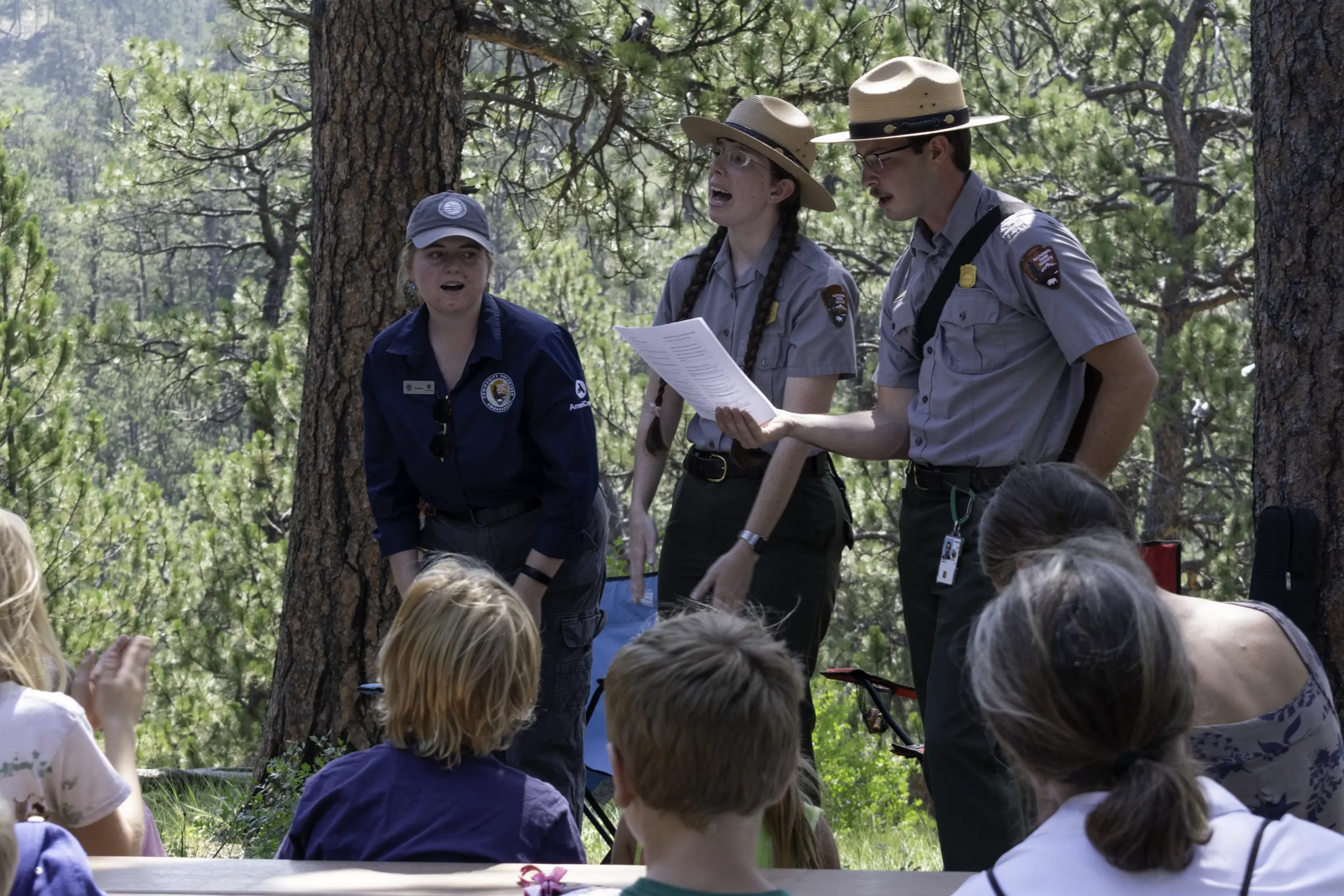 Park rangers lead a Junior Caver program outdoors, clapping and engaging a group of children.