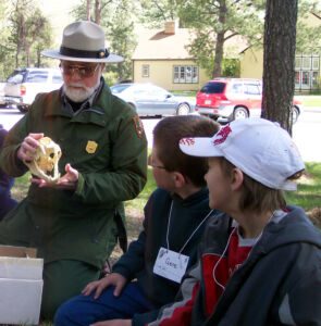 A park ranger holds a mock skull and is explaining it to two children