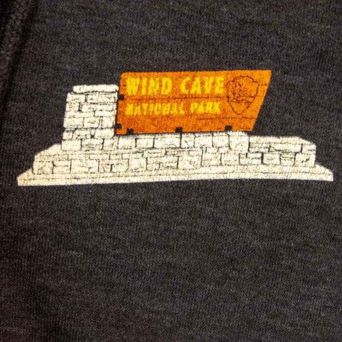 Close-up of the Wind Cave stone entrance sign and arrowhead printed on the hoodie left chest.