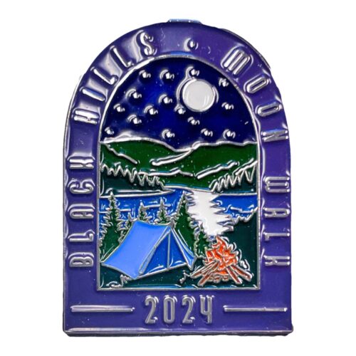 Arched enamel lapel pin with a purple border reading Black Hills Moon Walk in raised silver letters. Inside the arch, a night scene shows a full moon and stars above green hills, a lake, pine trees, a blue tent, and an orange campfire. The pin is dated 2024 at the bottom.