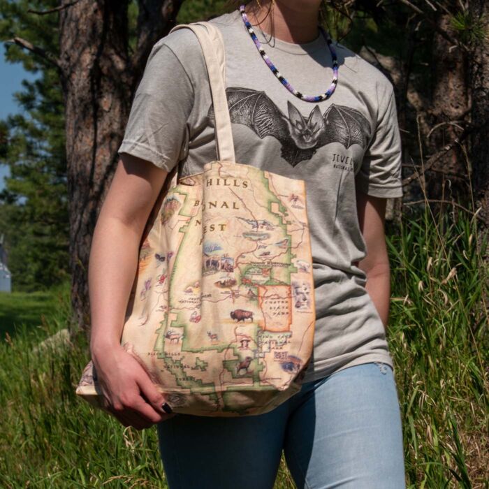 Person carrying the Black Hills map canvas tote bag on a pine-shaded trail