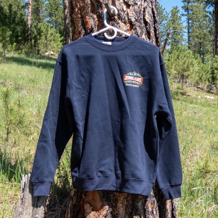 Navy Jewel Cave National Monument sweatshirt on a hanger in a Black Hills ponderosa pine forest, front view