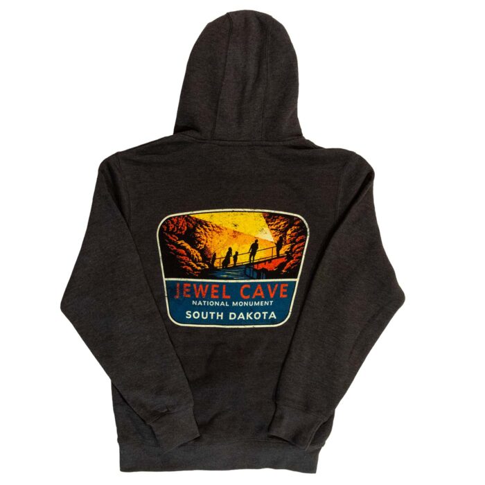 Back of the charcoal Jewel Cave National Monument full-zip hoodie, large faded sign with a cave-tour scene