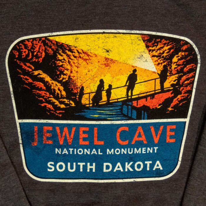 Close-up of the Jewel Cave National Monument back graphic, people in silhouette on a railed cave walkway under a shaft of light