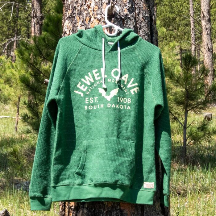 Heather green Jewel Cave National Monument pullover hoodie on a hanger in a Black Hills ponderosa pine forest