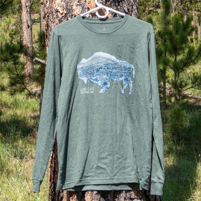 The heather green long-sleeve tee on a hanger against a ponderosa pine trunk in the Black Hills