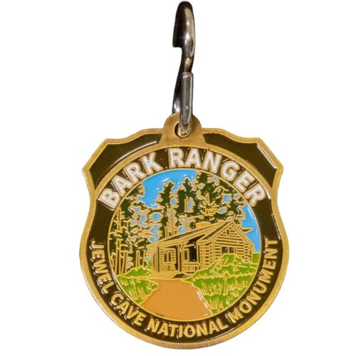 Jewel Cave National Monument BARK Ranger pet tag, front view showing historic cabin among ponderosa pines