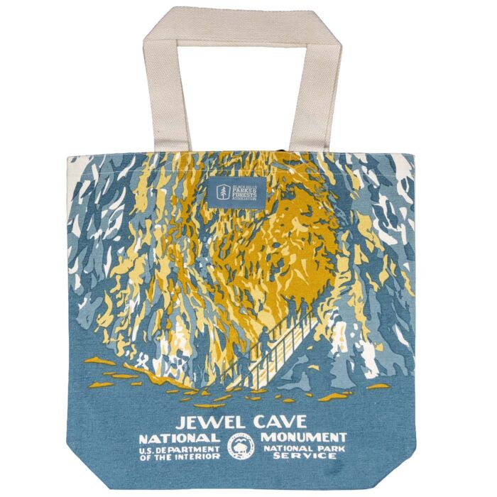 Natural canvas tote printed with a Jewel Cave chamber in gold and slate blue, a railed stairway of visitors climbing through it, with natural cotton handles.