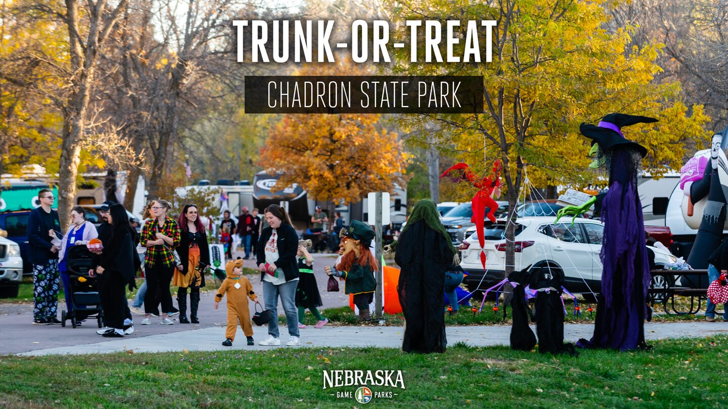 Families in costumes walk past Halloween decorations at a campground. Text reads: Trunk-or-treat. Chadron State Park. Nebraska Game and Parks.